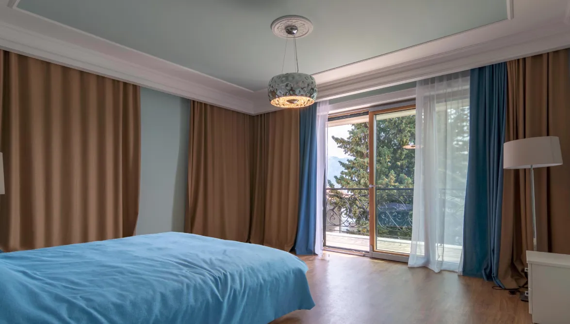Svijetla spavaća soba sa izlazom na balkon i plavim prekrivačem.
