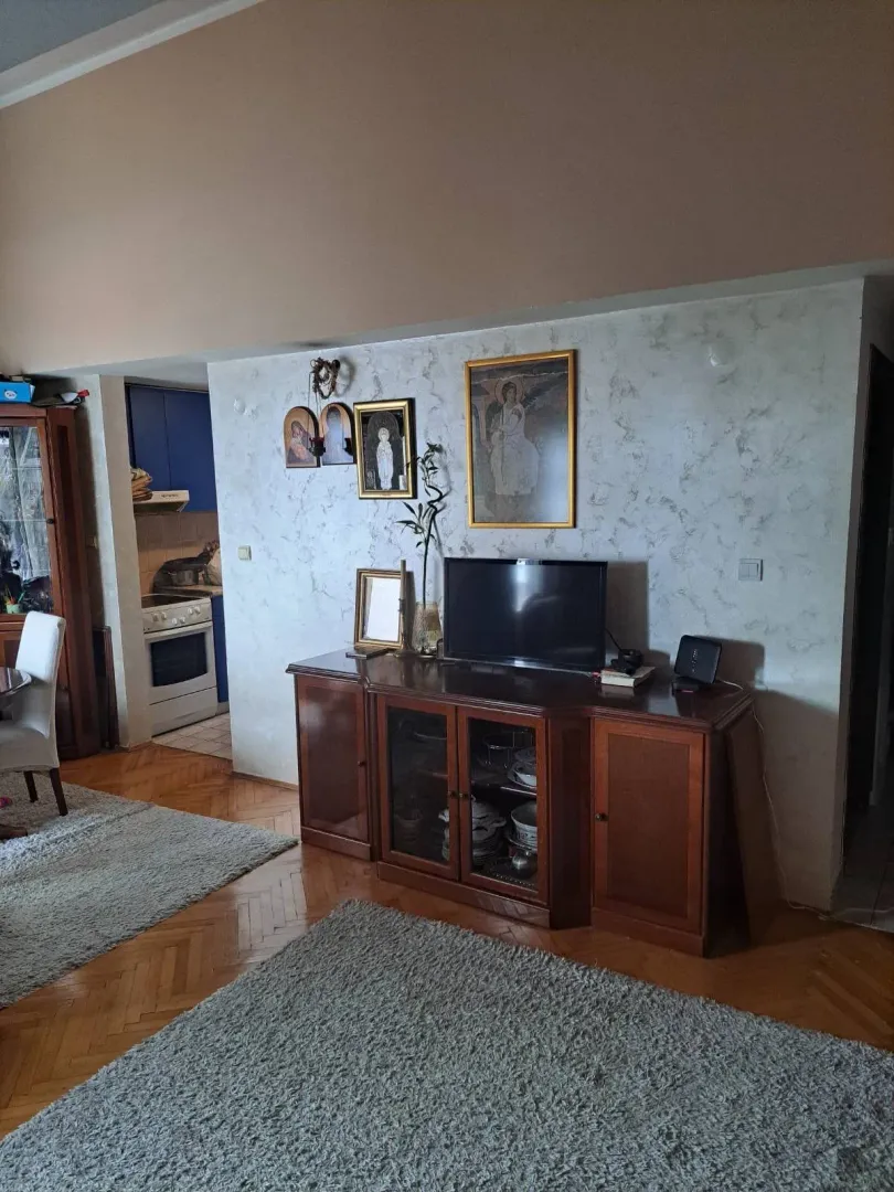 Dnevna soba sa drvenom komodom, televizorom i parketom na podu.