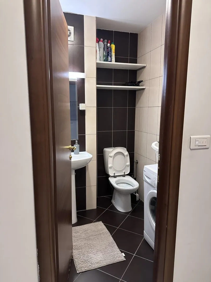 A bathroom with a toilet, sink, and washing machine seen through an open door.
