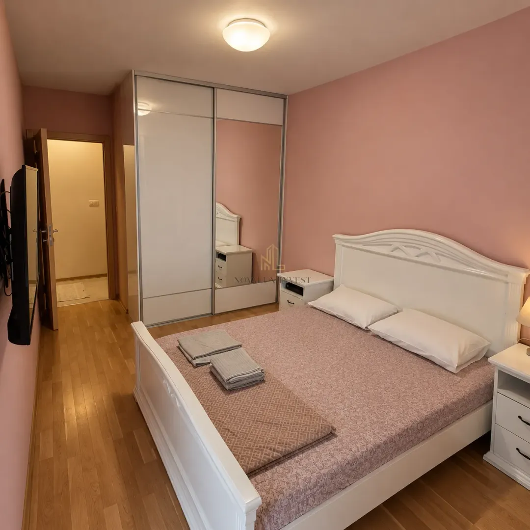Spavaća soba sa velikim bijelim krevetom, plakarom i ružičastim zidovima.