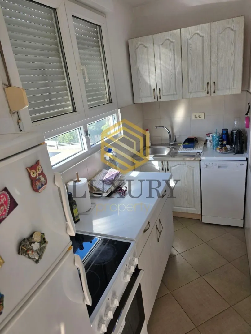 Small equipped kitchen with white cabinets and a window.