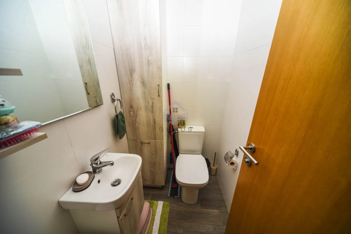 Manje kupatilo opremljeno umivaonikom, wc šoljom i ugradnim ormarićem.