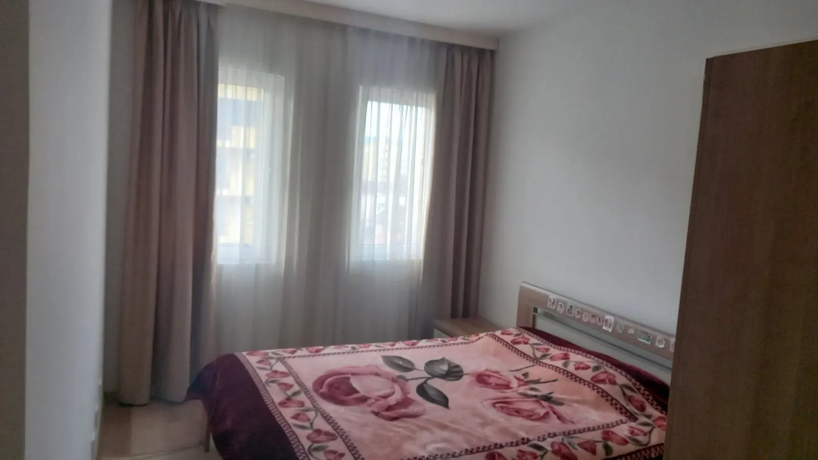 Jednostavna spavaća soba sa bračnim krevetom i zavjesama na prozorima.