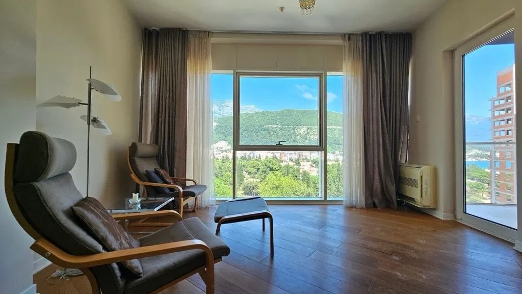 Living room with armchairs, wooden flooring, and large windows with a view of nature.