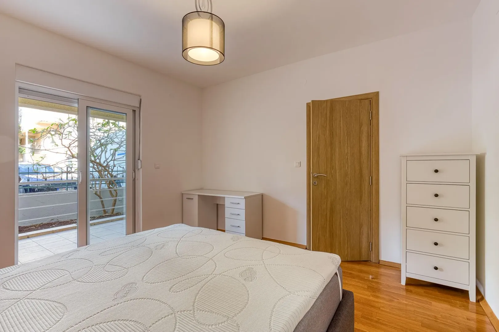 Bright bedroom with a bed, white dresser, and access to the terrace.