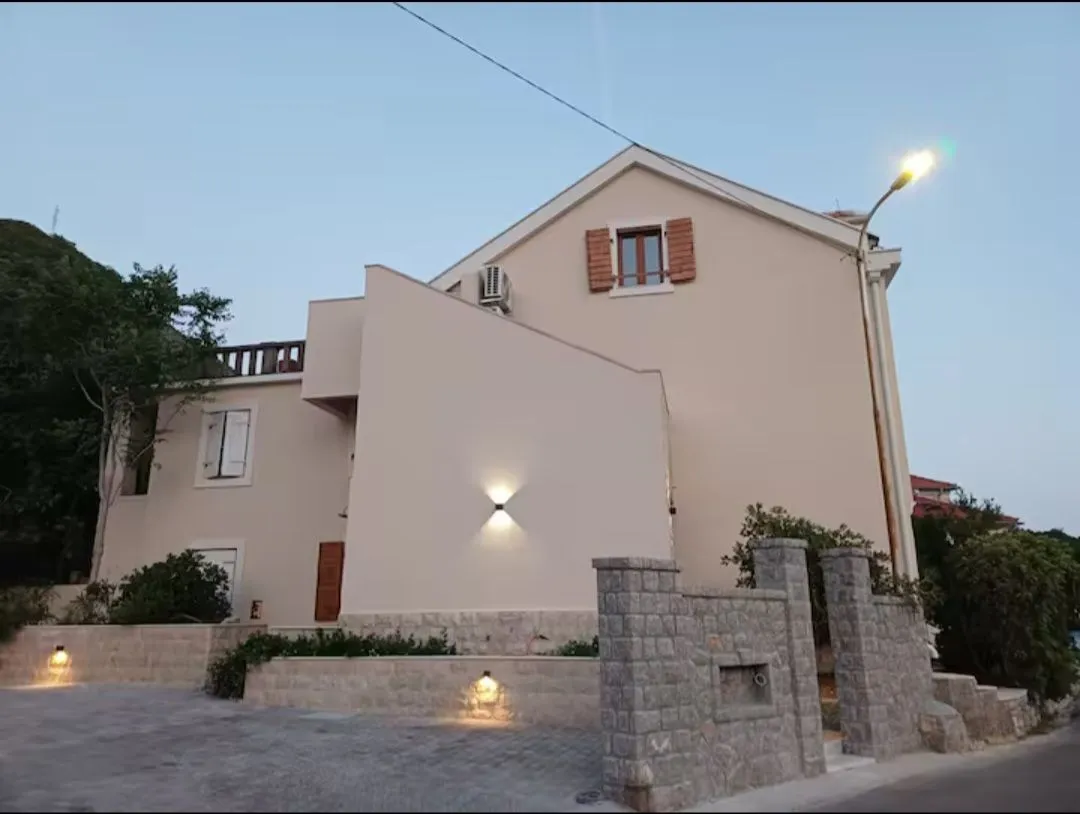 Eksterijer kuće sa dvorištem i rasvjetom u sumrak.