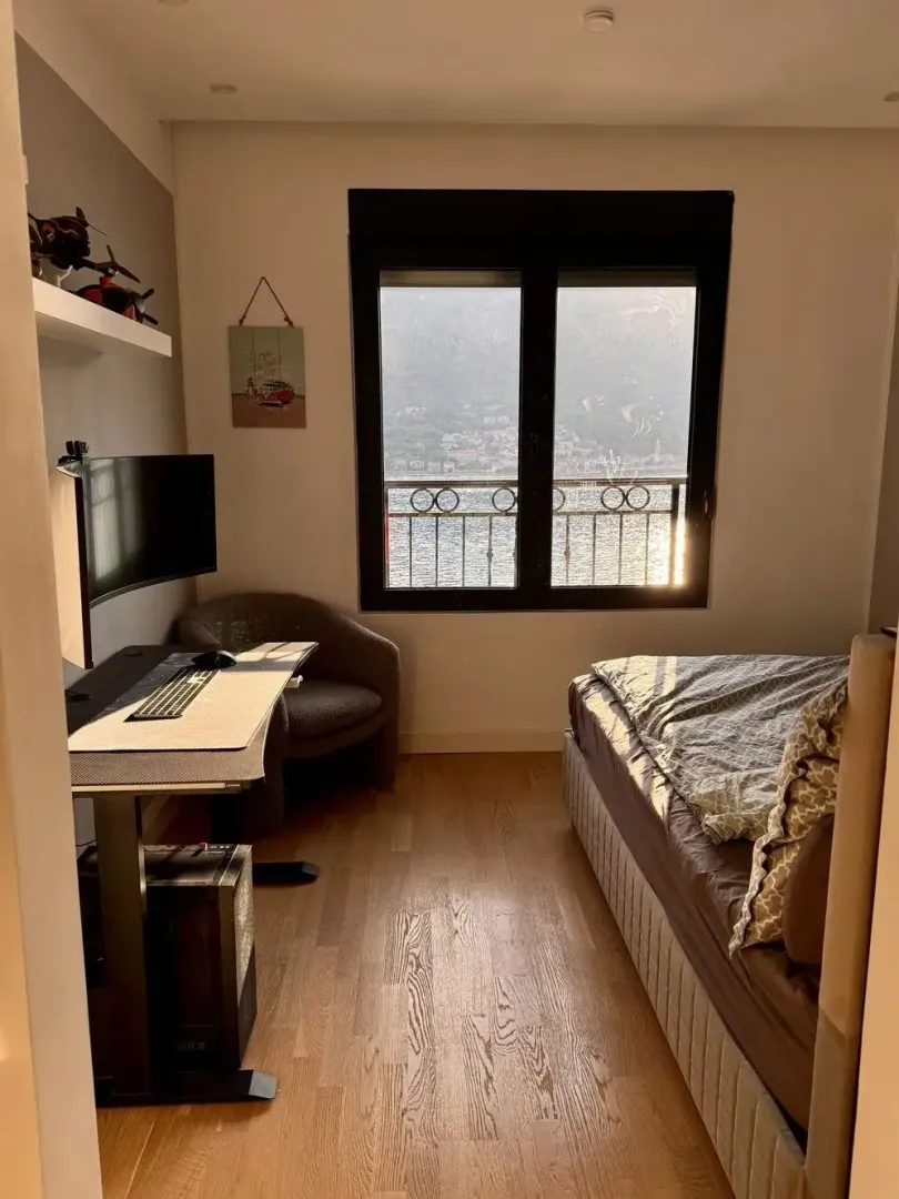 Manja spavaća soba sa krevetom, radnim stolom i pogledom na more.