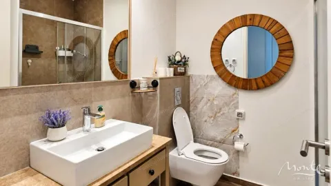 Savremeno opremljeno kupatilo sa umivaonikom, WC šoljom i ogledalom sa drvenim okvirom. - image 7