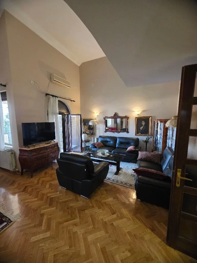 Spacious living room with seating furniture and parquet flooring.