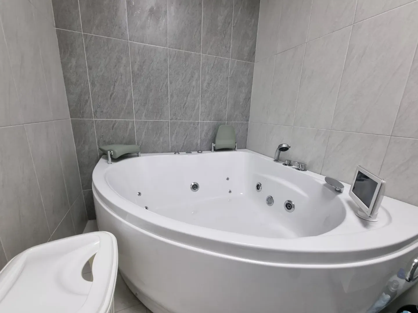 Kupatilo sa ugaonom hidromasažnom kadom i keramičkim pločicama na zidovima.