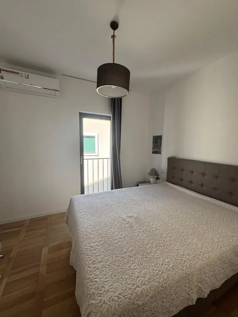 Furnished bedroom with a double bed, air conditioner, and balcony door.