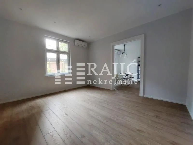 Empty room with laminate flooring and a window, looking into the dining area in the background.