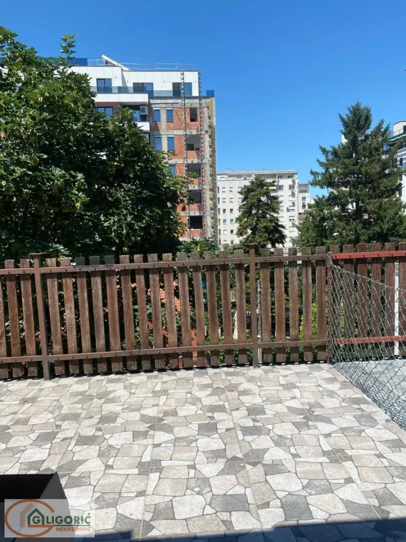Tiled terrace with a wooden fence and a view of surrounding buildings and greenery.