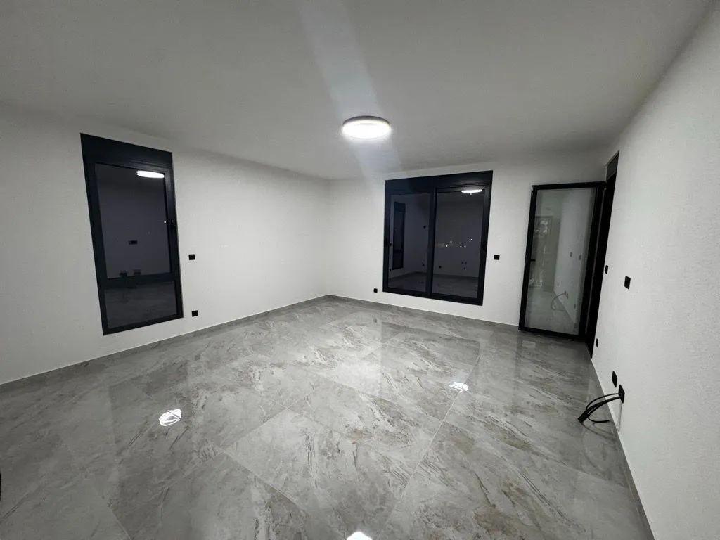An empty room with ceramic floor tiles and black window frames.