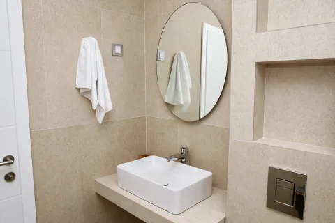 Moderno kupatilo sa umivaonikom, okruglim ogledalom i bež pločicama. - image 11