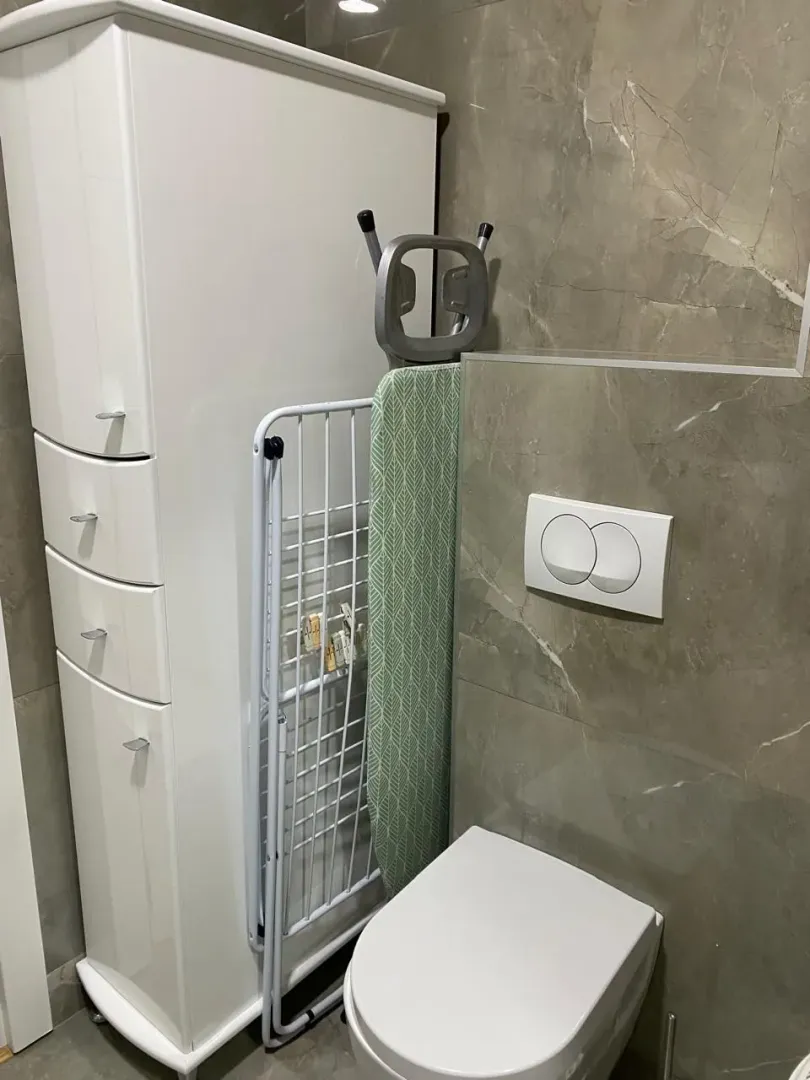 Manje uredno kupatilo sa WC šoljom, ormarićem i sušilicom za veš.