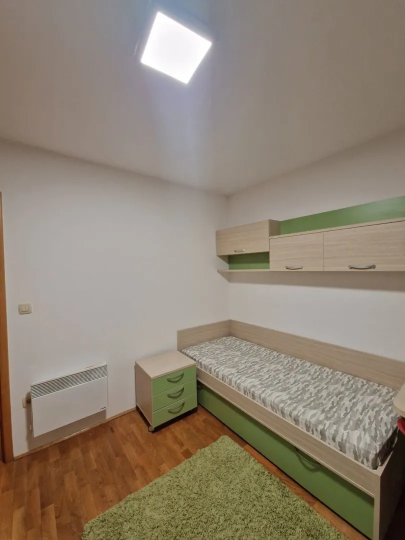 Jednostavna dječija soba sa krevetom, noćnim ormarićem i zelenim detaljima.
