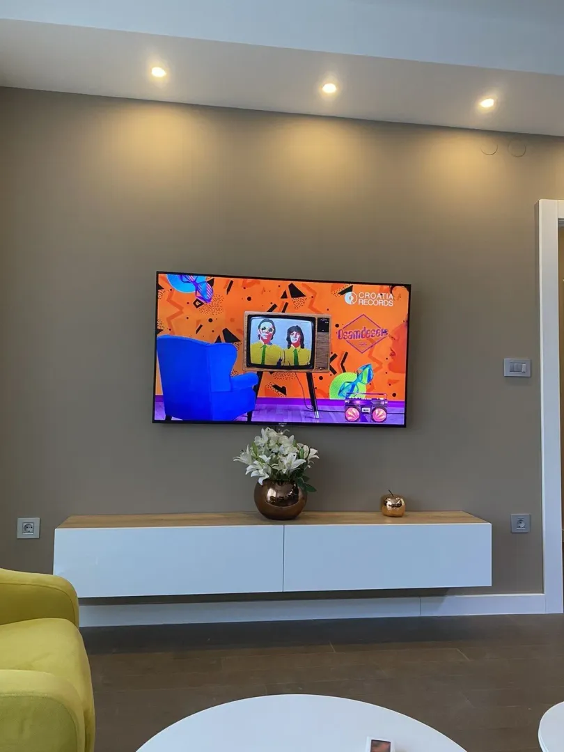 Zid u dnevnoj sobi sa televizorom i visećom komodom.