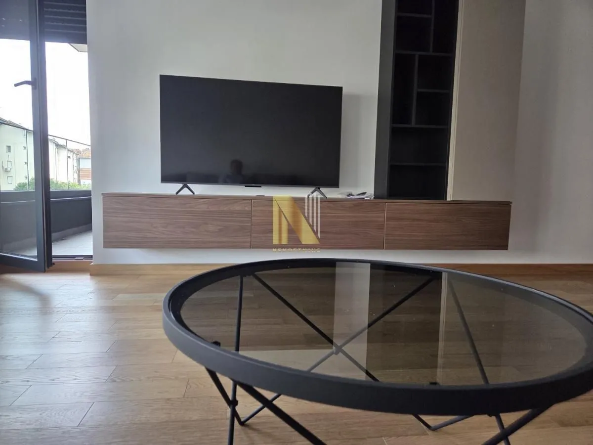 Dnevna soba sa televizorom, policama i okruglim stočićem.