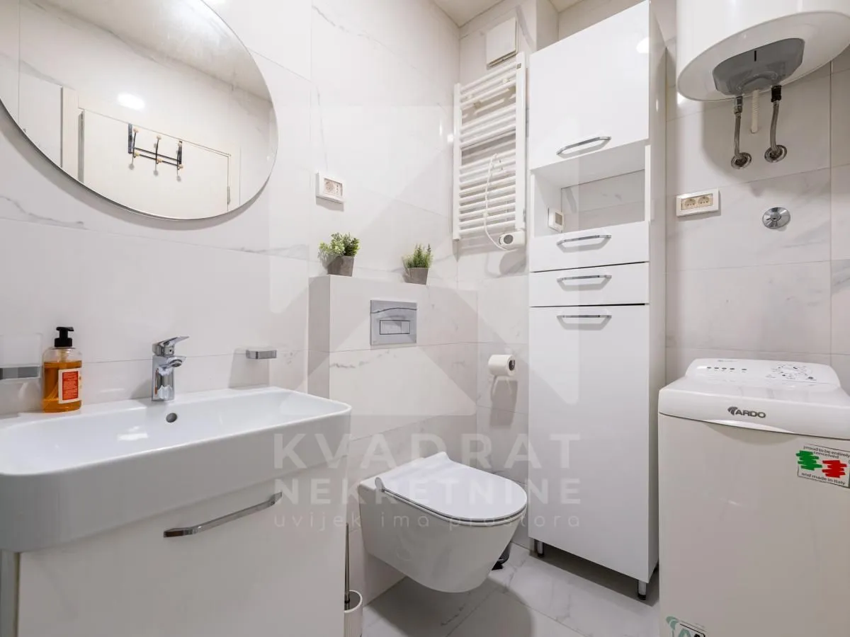 Kompaktno kupatilo sa bijelim namještajem, sanitarijama i veš mašinom.