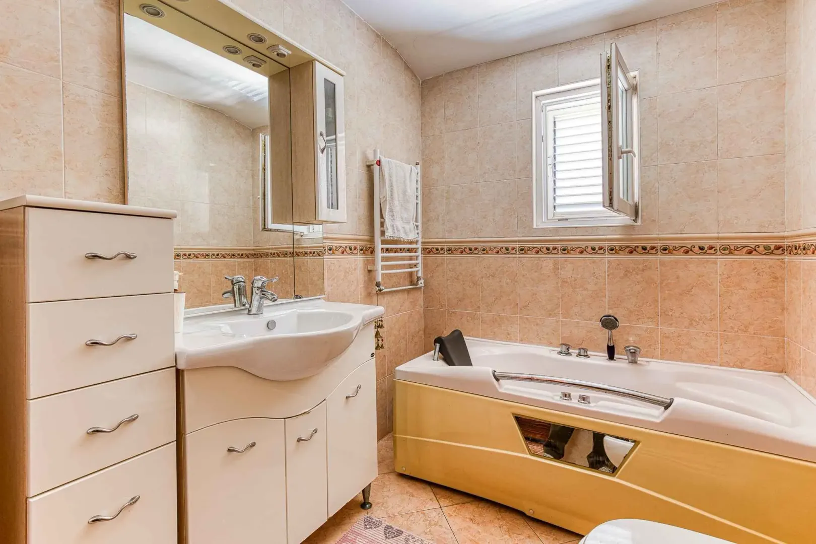 Kupatilo opremljeno umivaonikom, ormarićima, kadom i prozorom.
