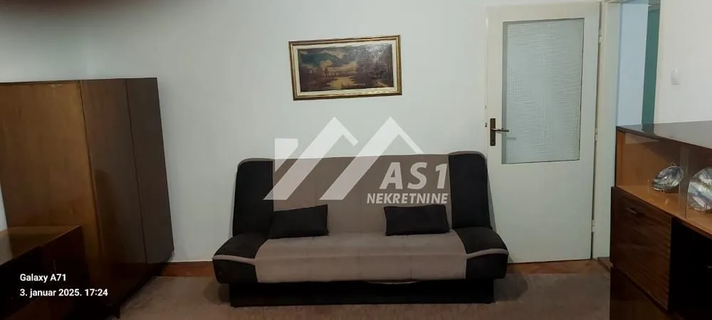 Dnevna soba sa kaučem, drvenim ormarom i slikom na zidu.