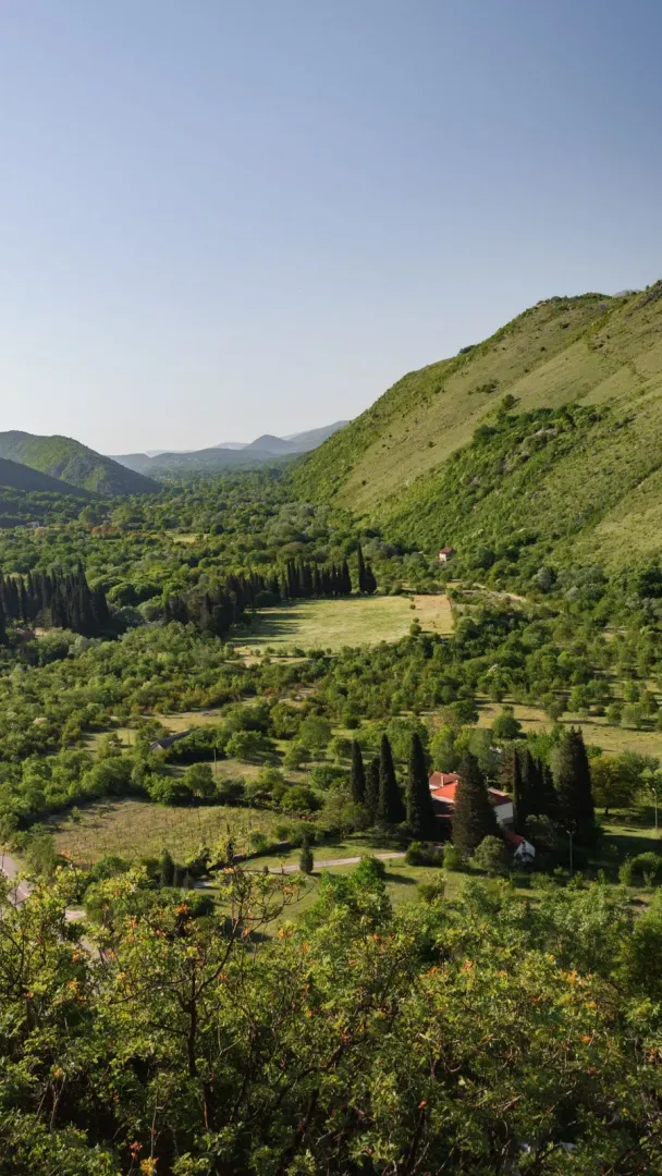Pogled na zelenu dolinu, brda i kuću sa okućnicom.