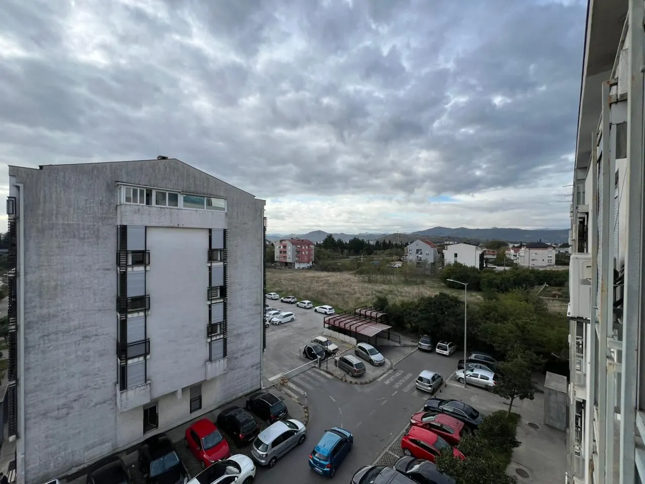 Pogled sa prozora na okolne zgrade i parking.