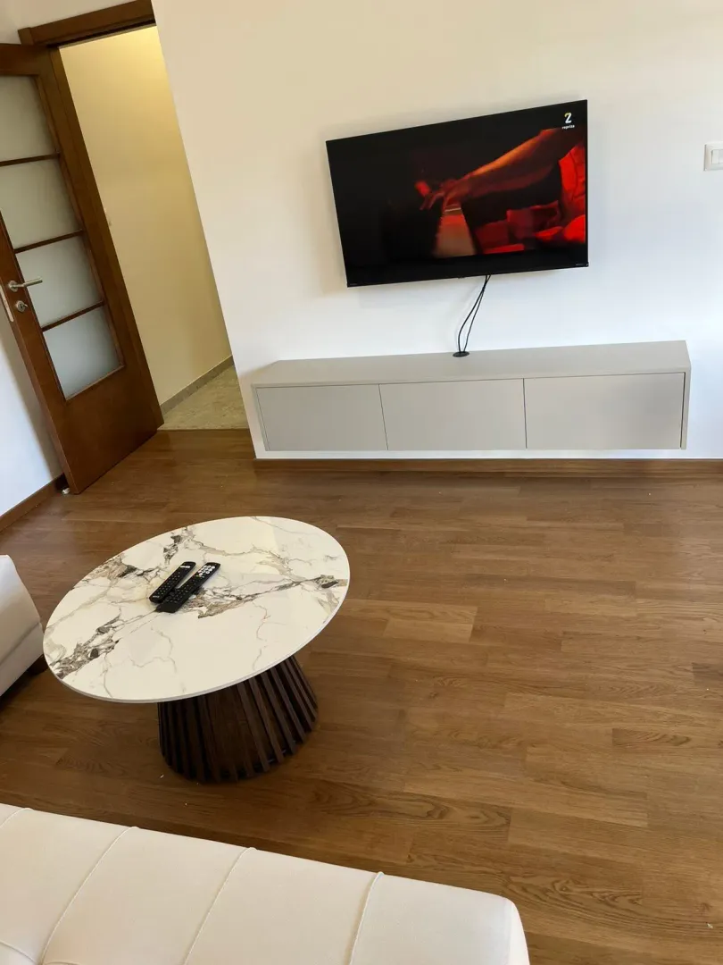 Dnevna soba sa TV-om na zidu i okruglim stočićem.