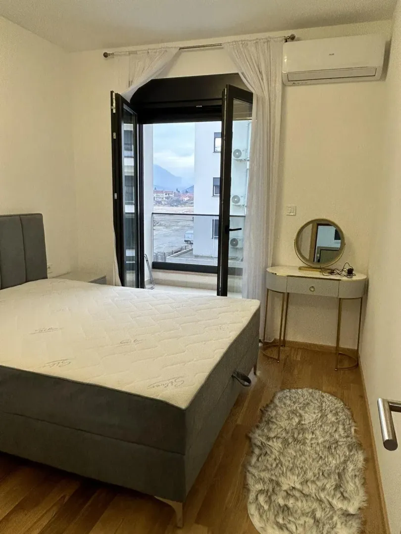 Svijetla spavaća soba sa bračnim krevetom, toaletnim stolom i izlazom na balkon.