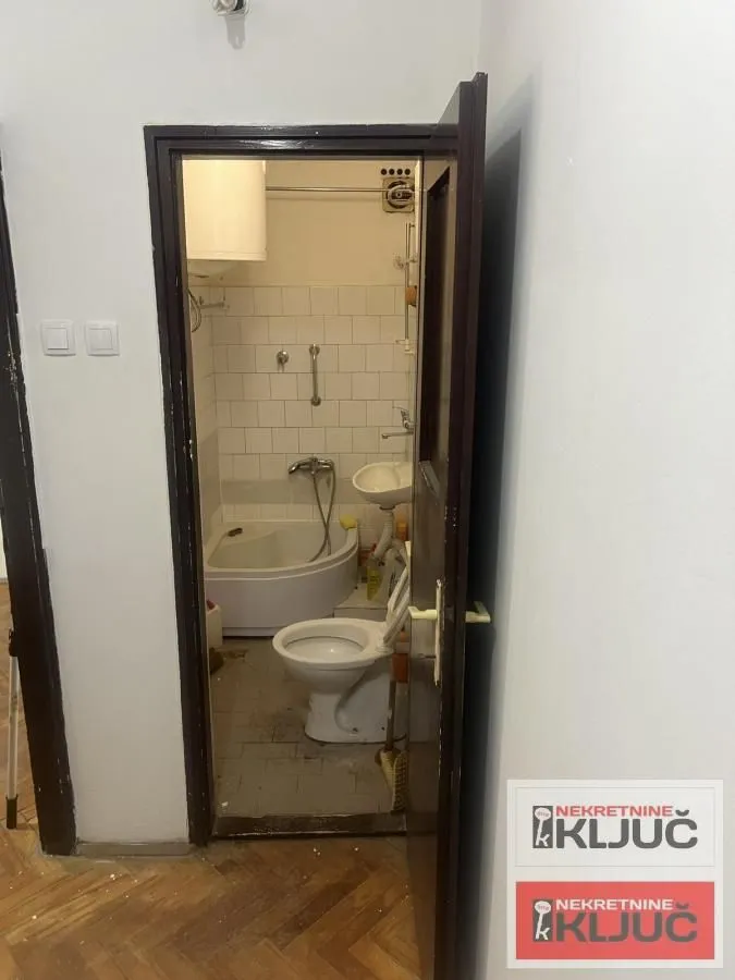 Pogled iz hodnika na manje kupatilo sa kadom i toaletom.