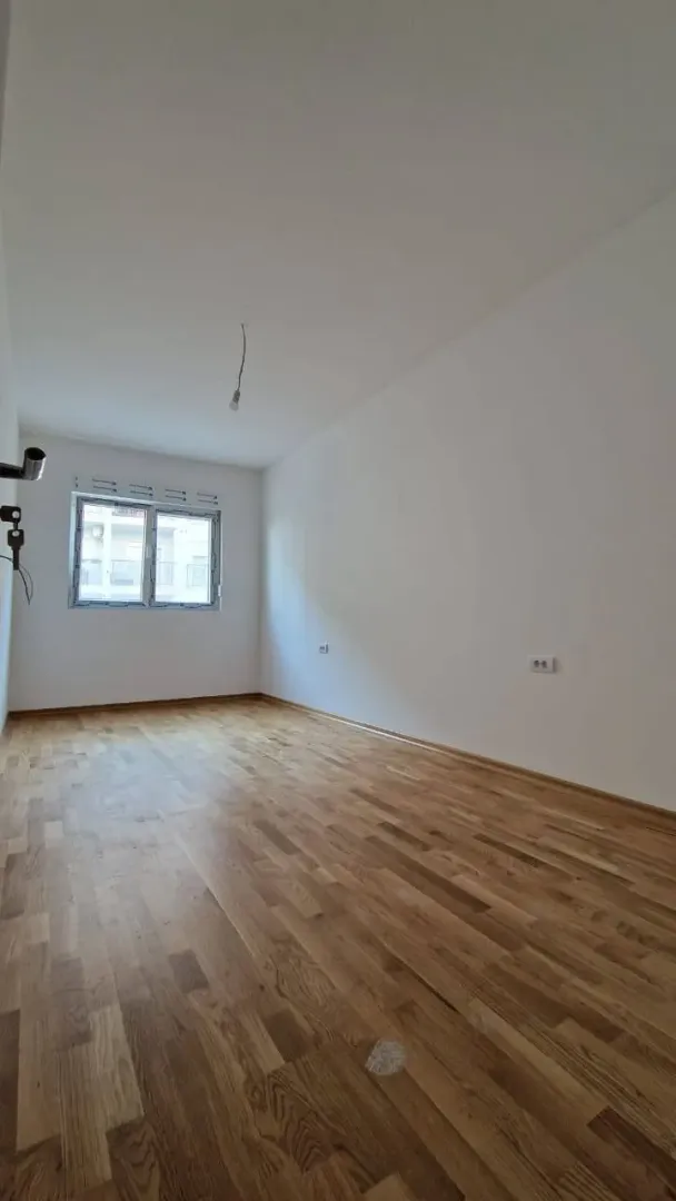 Prazna soba sa parketom i jednim prozorom.