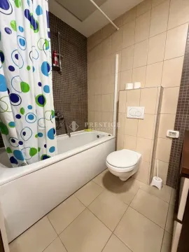 Pregledno kupatilo sa kadom, toaletom i bež pločicama. - image 10