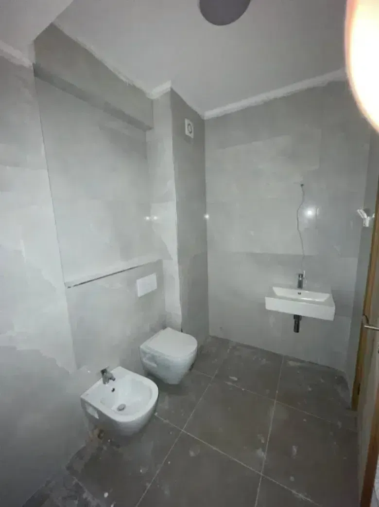 Novoopremljeno kupatilo sa sivu keramikom, umivaonikom i sanitarijama.