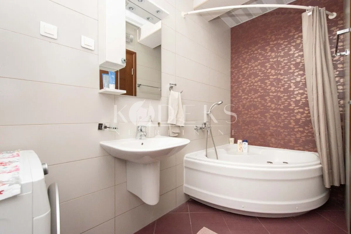 Bathroom equipped with a washbasin, corner bathtub, and washing machine.