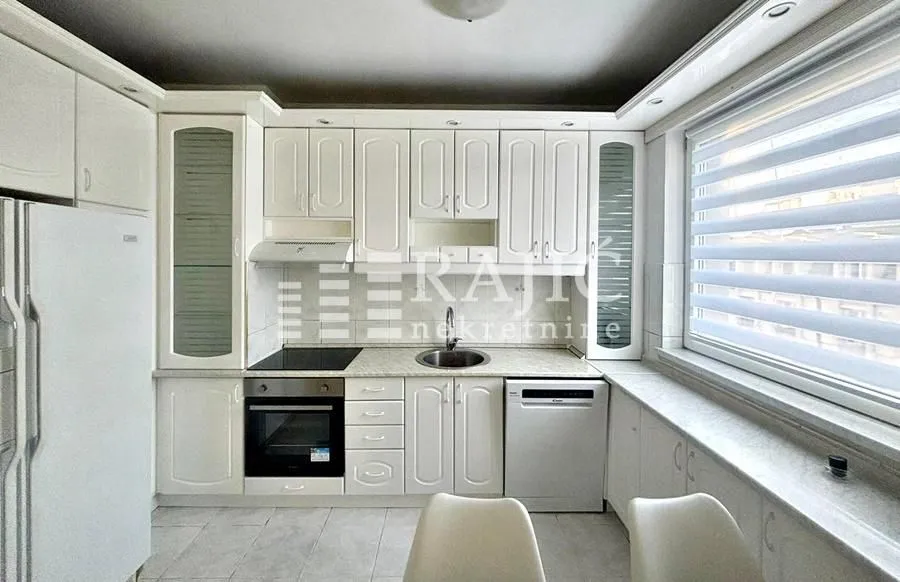 White kitchen with built-in appliances and a window.