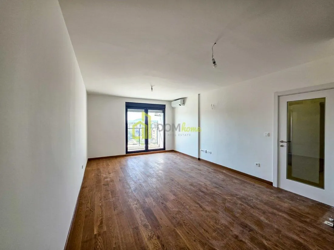 Empty unfurnished room with wooden flooring and balcony doors.