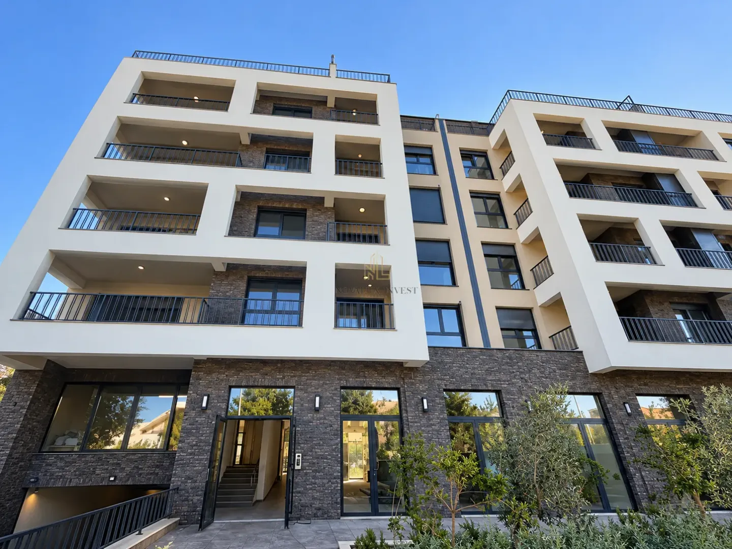 Pogled na spoljašnjost moderne stambene zgrade sa terasama i uređenim ulazom.