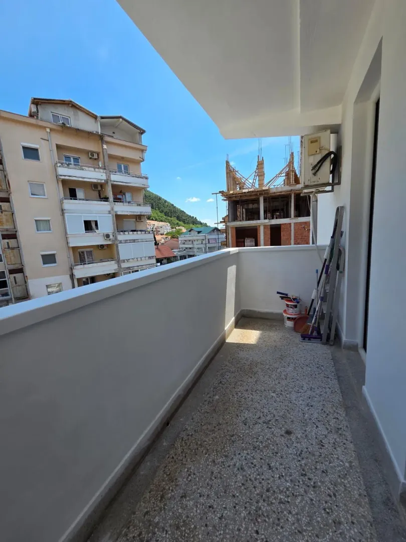 Prazan balkon sa pogledom na okolne zgrade i brdo.