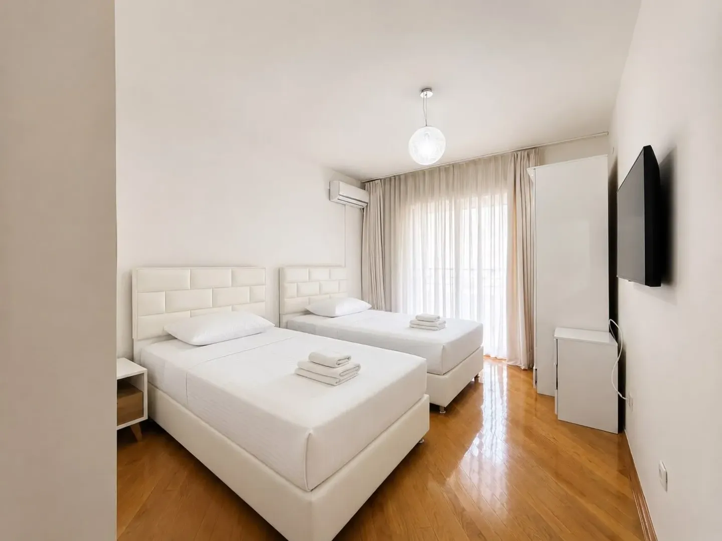 Bright bedroom with two single beds and hardwood flooring.
