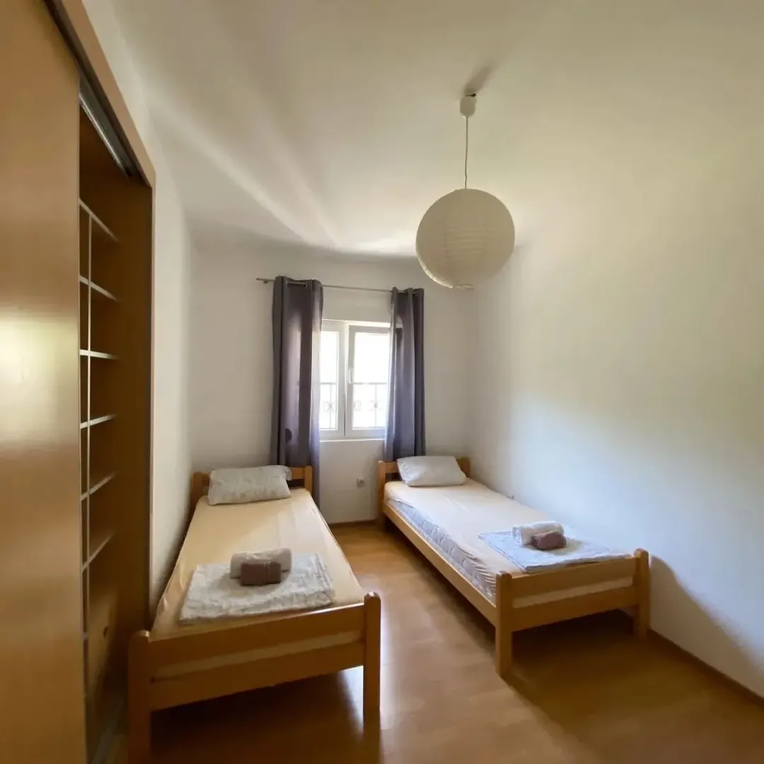 Spavaća soba sa dva odvojena kreveta, ormarom i prozorom.