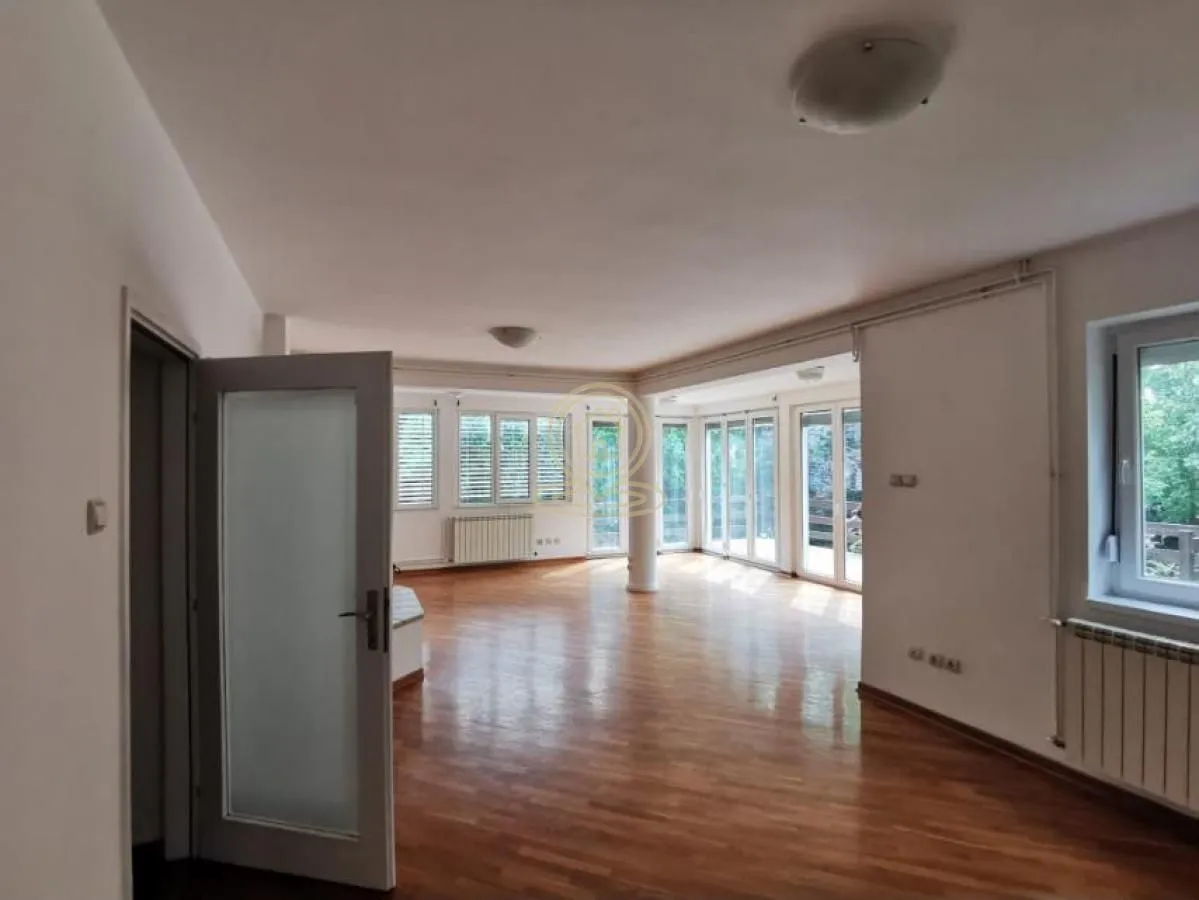 Spacious empty living room with parquet flooring and large windows.