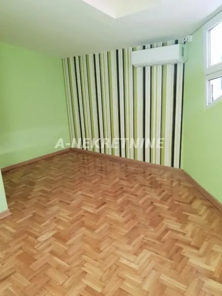 Prazna soba sa parketom na podu i klima uređajem na zidu.