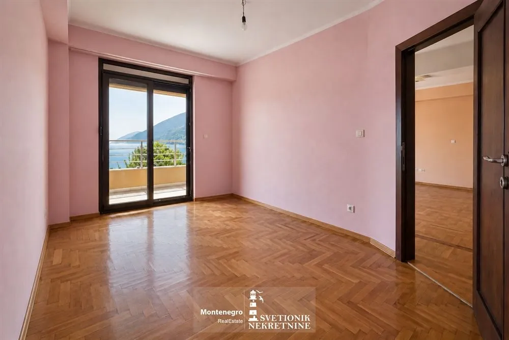 Prazna soba sa roze zidovima, parketom i izlazom na terasu sa pogledom na more.