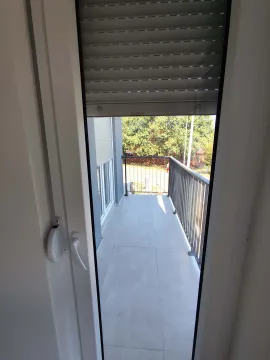 View of a covered balcony with tiled flooring and a metal railing through an open balcony door with roller shutters. - image 18