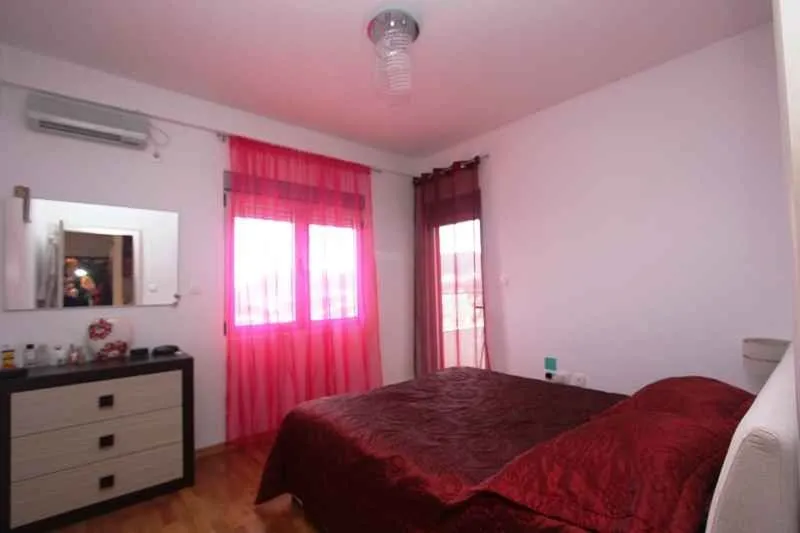 Spavaća soba sa bračnim krevetom, komodom i jarkoružičastim zavjesama.