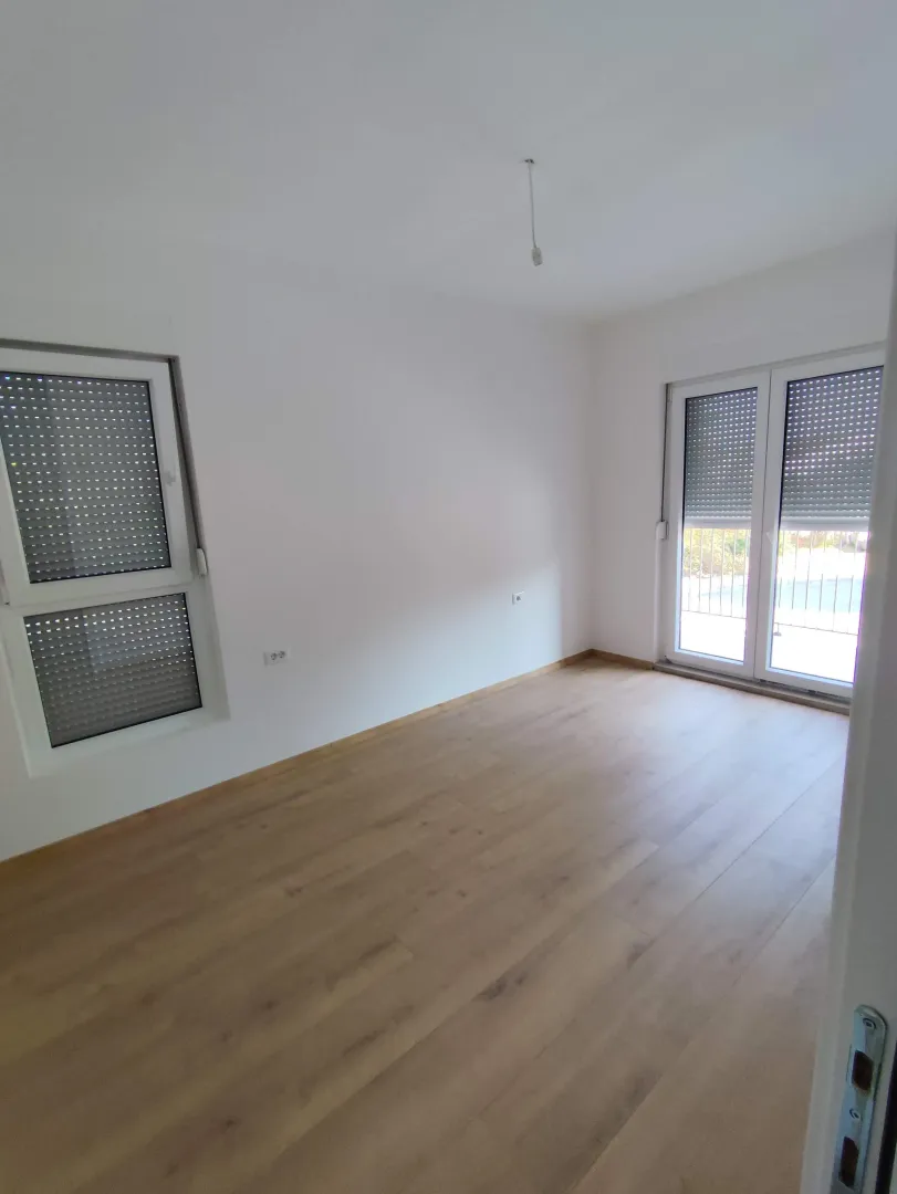 Empty bright room with hardwood flooring and windows with roller shutters.
