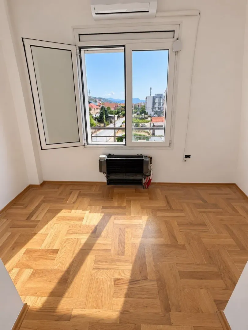 Empty room with parquet flooring, an open window, and a view of the surroundings.