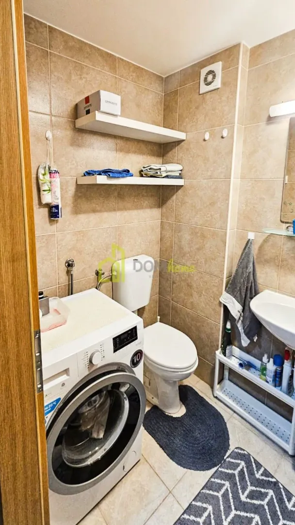 Small tiled bathroom with a toilet, washbasin, and washing machine.