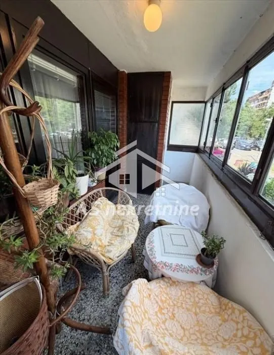 Enclosed balcony with seating furniture and houseplants.